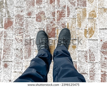 A man's feet on paving slabs covered with snow.