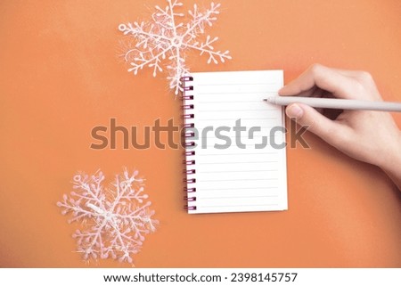 Top view of child hand with holding pen on white paper blank notebook and writing wish list.