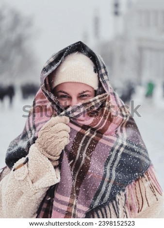 A beautiful girl in winter clothes and a warm scarf has taken refuge from the frost of the wind and blizzard, walking through the winter city