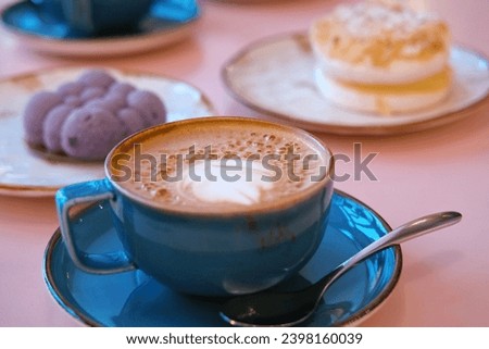 Cup of Cappuccino with Art Milk Foam Top View. Latte with Steel Spoon. Hot Coffee in a Blue Ceramic Mug With Saucer on a Pink Table. Modern Glamour Coffee Shop, Cafeteria. Thick Froth. No People. 4K Royalty-Free Stock Photo #2398160039