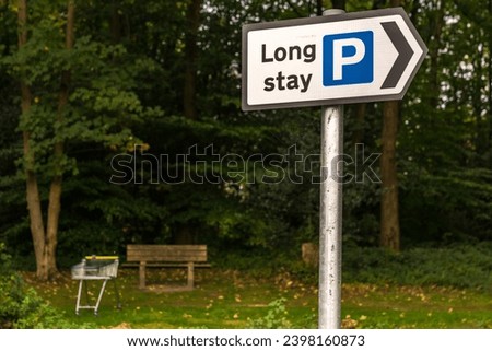 Sign: Long stay parking, with a bench and a shopping trolley in the background, seen in Crowborough, East Sussex, England, UK