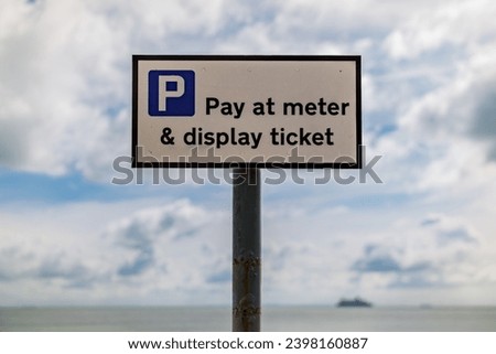 Sign: Pay at meter and display ticket, seen in St Margaret's at Cliffe, Kent, England, UK - with clouds and a ferry crossing the British channel in the background
