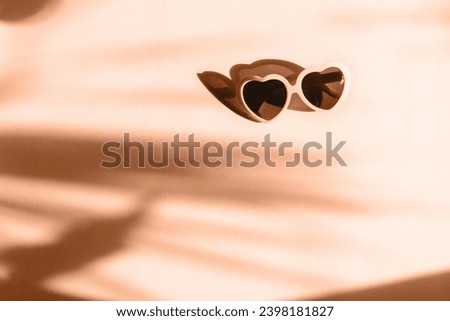 Trendy Peach Fuzz pantone color of Year 2024 background. Heart sunglasses on bright light peach background