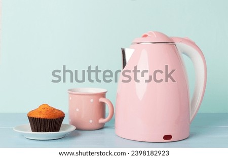 Pink electric kettle with cup of tea and dessert on table