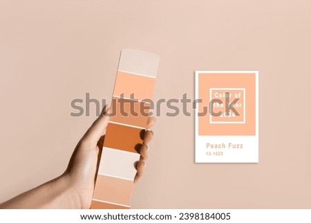 Hand holding Color samples palette design catalog. New trending PANTONE 13-1023 Peach Fuzz colour of 2024 year  Royalty-Free Stock Photo #2398184005