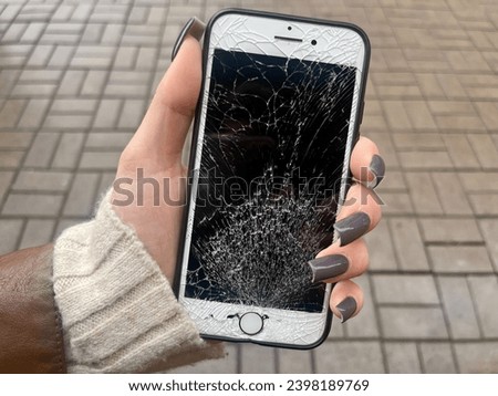 A young girl holds in her hand a mobile phone with a broken screen on the background of the street.