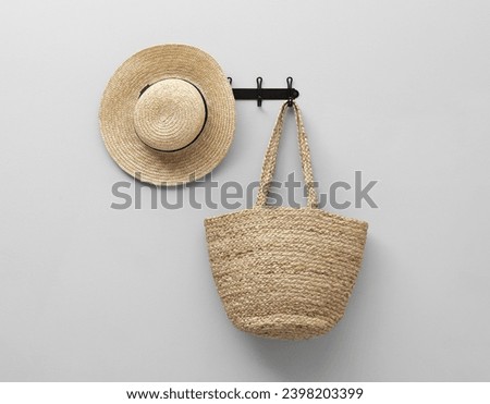Straw hat and bag hanging on rack on light grey wall