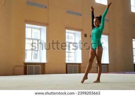 Full shot of girl gymnast wearing green leotard with hands up exercising on gym floor, copy space