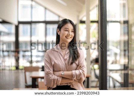 Portrait of happy asian businesswoman standing arms crossed in office. Looing outside mirror.