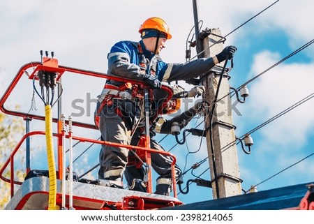 Two professional electricians in hard hats are repairing power lines from cradle of bucket truck. View from below. Electricians change cables on street lighting poles. Royalty-Free Stock Photo #2398214065