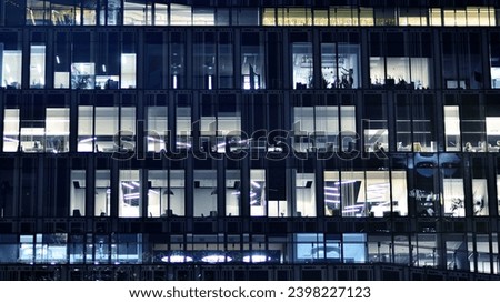 Fragment of the glass facade of a modern corporate building at night. Modern glass office  in city. Big glowing windows in modern office buildings at night, in rows of windows light shines. 