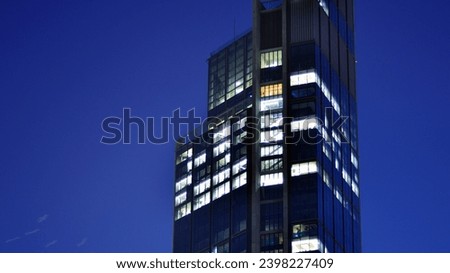 The glass facade of a modern skyscraper at night. Modern glass office in city. Big glowing windows in modern office building at night. In rows of windows light shines.
