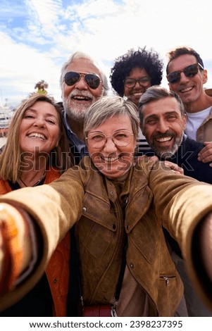 Cheerful vertical selfie of a group of mature people looking at camera happily, taking photos during their family trip together.