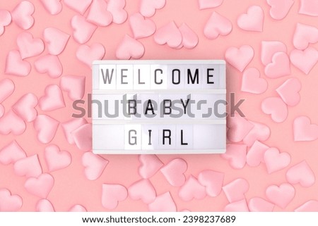 Welcome baby girl. Lightbox with letters and confetti in a heart shape on a pink background. 