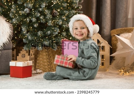 A beautiful little boy looks into the magic box under the Christmas tree. A New Year's gift. The concept of celebrating Christmas and New Year 2024.
