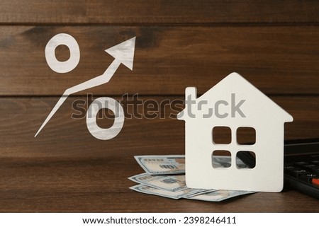 Mortgage rate rising illustrated by percent sign with upward arrow. House model, money and calculator on wooden table