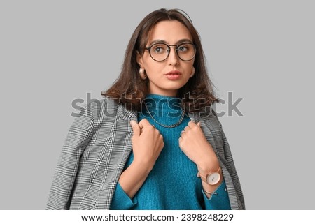 Fashionable young woman with stylish jewellery and eyeglasses on grey background