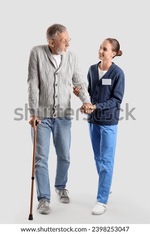 Senior man with walking stick and nurse on light background Royalty-Free Stock Photo #2398253047