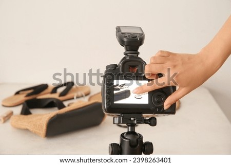 Female photographer taking photo of flip-flops, bag and hat in studio