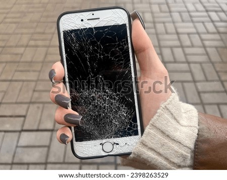 A young girl holds in her hand a mobile phone with a broken screen on the background of the street. Vertical photo. 