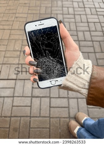 A young girl holds in her hand a mobile phone with a broken screen on the background of the street. Vertical photo. 