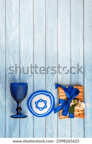 Pesah jewish Passover holiday celebration concept. Jewish kippah with a Star of David, matzah, wineglass, blooming jasmine. Blue wooden background with empty copy space. Royalty-Free Stock Photo #2398265625