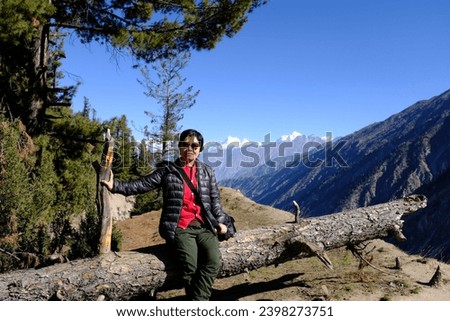An asian female tourist sitting on a large fallen tree admiring the scenic view of high mountains on Fairy Meadows on Karakoram Highway, Pakistan.