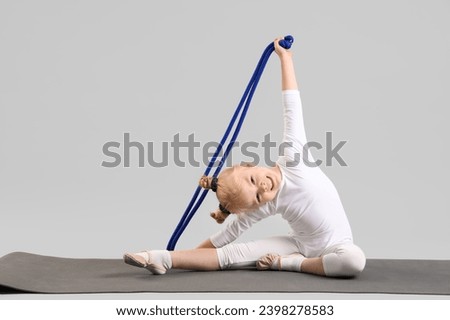 Cute little girl with rope doing gymnastics on mat against light background