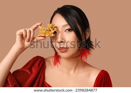 Beautiful young Asian woman with golden dragon figurine on brown background. Chinese New Year celebration