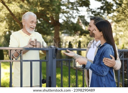 Friendly relationship with neighbours. Happy couple and senior man near fence outdoors Royalty-Free Stock Photo #2398290489