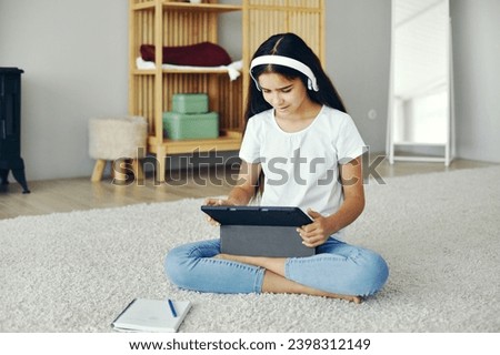 Pretty pre-teen girl sit on floor in cozy living room wear wireless headphones studying online use digital tablet device. Self-education, younger gen and modern tech usage for learning, gain new skill