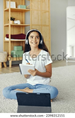 Pretty pre-teen girl sit on floor in cozy living room wear wireless headphones studying online use digital tablet device. Self-education, younger gen and modern tech usage for learning, gain new skill Royalty-Free Stock Photo #2398312151