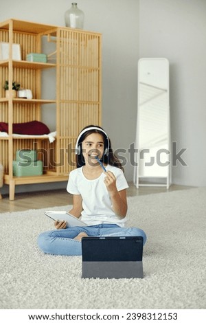 Pretty pre-teen girl sit on floor in cozy living room wear wireless headphones studying online use digital tablet device. Self-education, younger gen and modern tech usage for learning, gain new skill Royalty-Free Stock Photo #2398312153