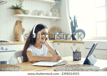 Pretty pre-teen 12s girl in wireless headphones sit at table e-learning, listen on-line course, audio lesson, receive new knowledge, skills using internet and modern tech. Child development. Education Royalty-Free Stock Photo #2398314551