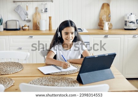 Pretty pre-teen 12s girl in wireless headphones sit at table e-learning, listen on-line course, audio lesson, receive new knowledge, skills using internet and modern tech. Child development. Education Royalty-Free Stock Photo #2398314553