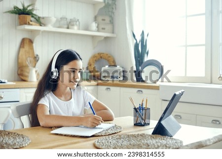 Pretty pre-teen 12s girl in wireless headphones sit at table e-learning, listen on-line course, audio lesson, receive new knowledge, skills using internet and modern tech. Child development. Education Royalty-Free Stock Photo #2398314555