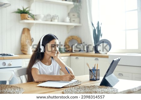 Pretty pre-teen 12s girl in wireless headphones sit at table e-learning, listen on-line course, audio lesson, receive new knowledge, skills using internet and modern tech. Child development. Education Royalty-Free Stock Photo #2398314557