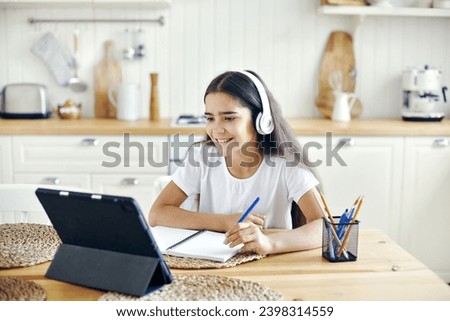 Pretty pre-teen 12s girl in wireless headphones sit at table e-learning, listen on-line course, audio lesson, receive new knowledge, skills using internet and modern tech. Child development. Education Royalty-Free Stock Photo #2398314559