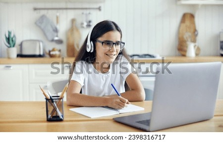 Pre-teen 12s girl in headphones and eyeglasses sit at table e-learns, listen online course, audio lesson, get new knowledge, skills using internet and modern tech. Development, education, eye-sight Royalty-Free Stock Photo #2398316717