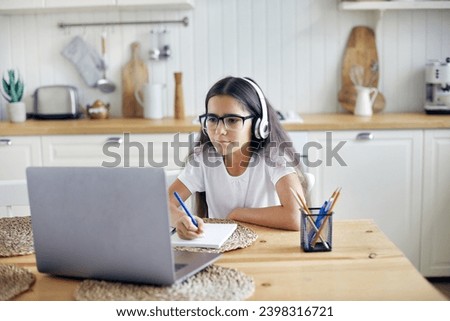 Pre-teen 12s girl in headphones and eyeglasses sit at table e-learns, listen online course, audio lesson, get new knowledge, skills using internet and modern tech. Development, education, eye-sight Royalty-Free Stock Photo #2398316721