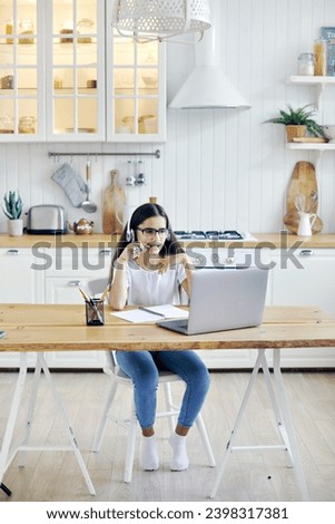 Pre-teen 12s girl in headphones and eyeglasses sit at table e-learns, listen online course, audio lesson, get new knowledge, skills using internet and modern tech. Development, education, eye-sight Royalty-Free Stock Photo #2398317381