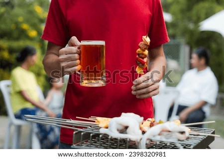 Barbecue with grilled chicken and sausages. People in casual clothes are cooking and holding a glass of beer.