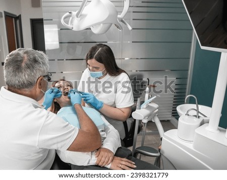 The photo shows how professional teeth cleaning ensures their impeccable cleanliness. A woman at an appointment at a dental center A dentist and his assistant work closely on the condition of the Royalty-Free Stock Photo #2398321779