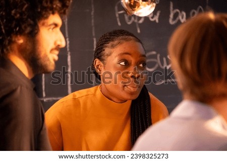 The image captures a moment of engaging discussion among three individuals. The central figure, a woman in a mustard-yellow top, is the focal point, with her expressive eyes wide and lips pursed Royalty-Free Stock Photo #2398325273
