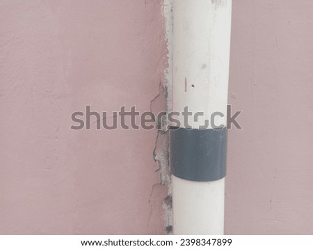White pvc pipe clamped on a faded pink wall. suitable for texture and background themes.