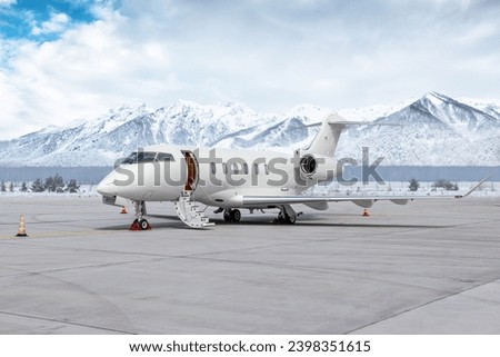 Modern white executive jet plane with an opened gangway door at the winter airport apron on the background of high scenic snow capped mountains Royalty-Free Stock Photo #2398351615