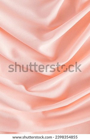 Soft pleats of peach colored satin textiles. Luxury abstract textile background design. Vertical view. Color of the Year 2024 peachy fuzz