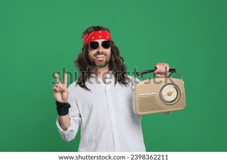 Stylish hippie man in sunglasses with retro radio receiver showing V-sign on green background