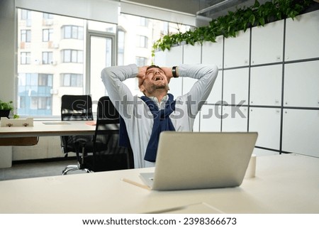 Emotional man with a laptop sits at large office table Royalty-Free Stock Photo #2398366673