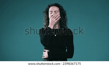 Exhausted person covers mouth yawning showing signal of fatigue standing on teal background
